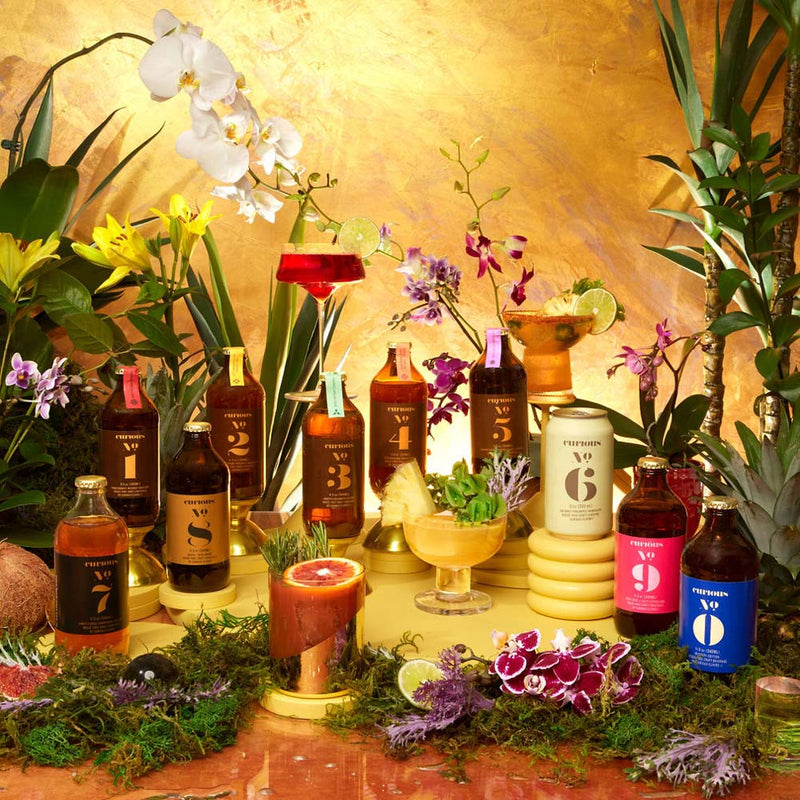 Assorted bottles of Curious Elixirs with decorative elements on a table against a gold background