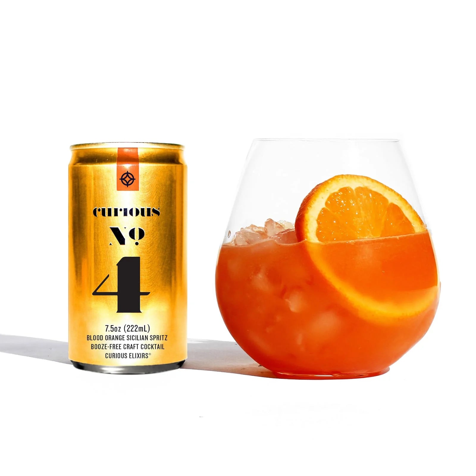 Mini Gold can of 'Curious No. 4' next to a glass of orange cocktail with an orange slice on a white background