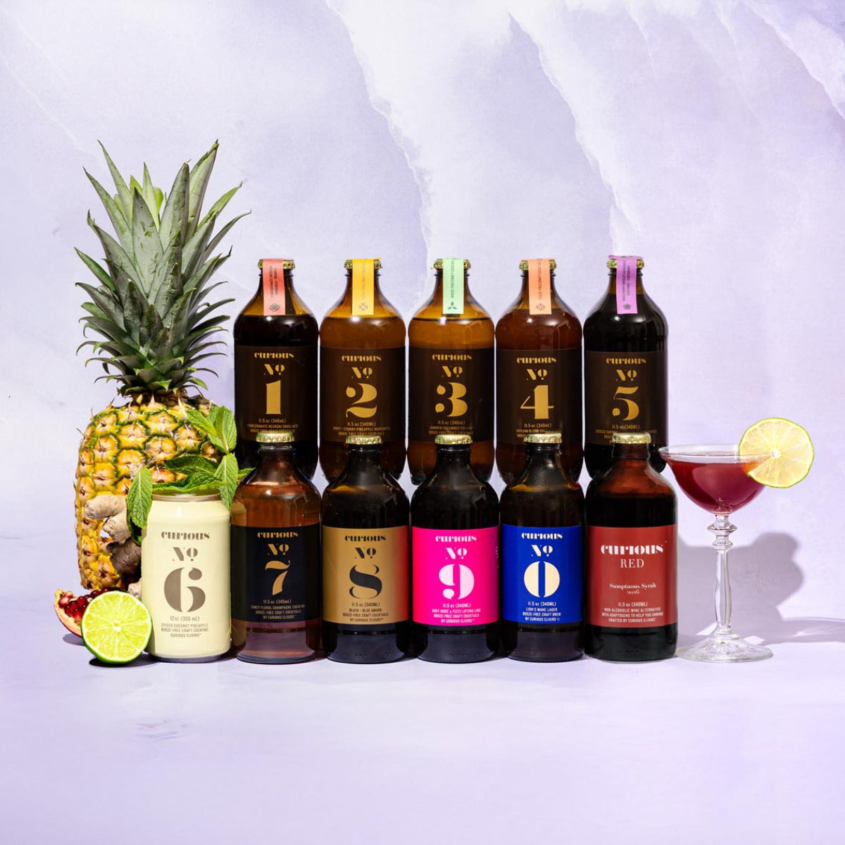 Collection of Curious Elixirs bottles and a pineapple on a light purple background